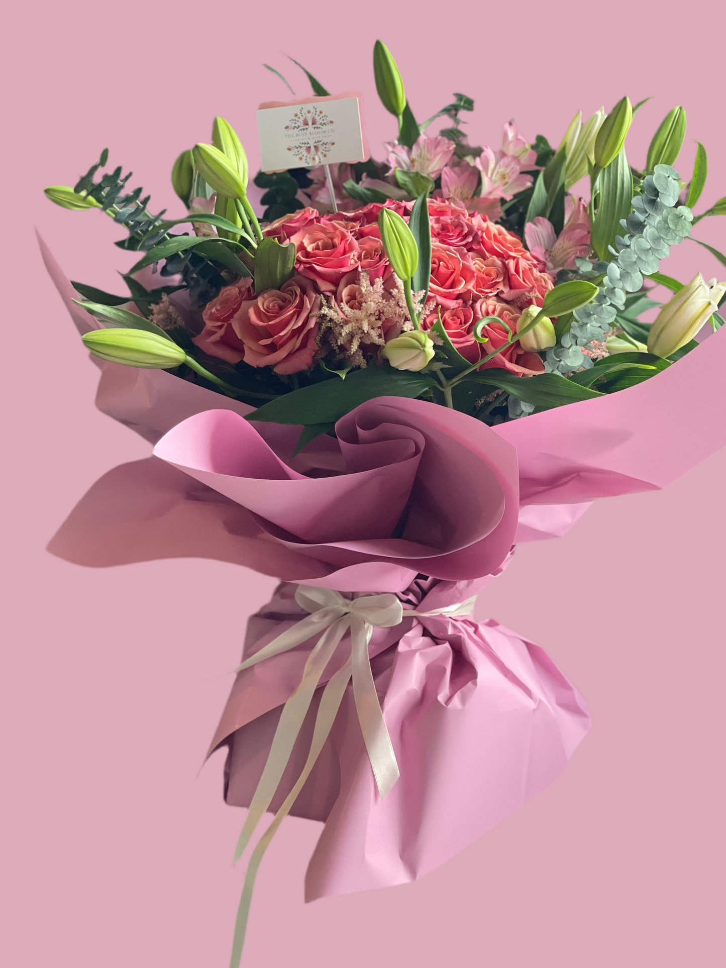 Bouquet of flowers wrapped in pink paper on a pink background
