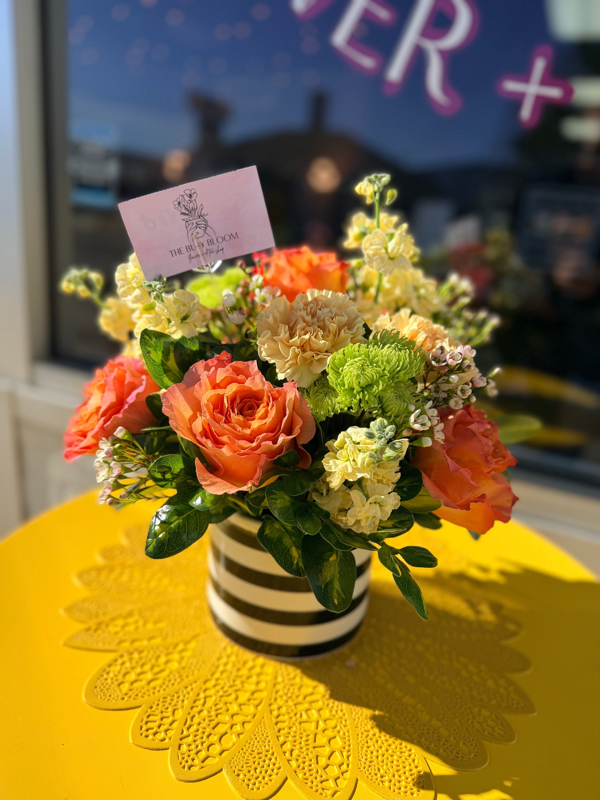 Floral arrangement in a striped vase on a yellow tablecloth with a blurred background
