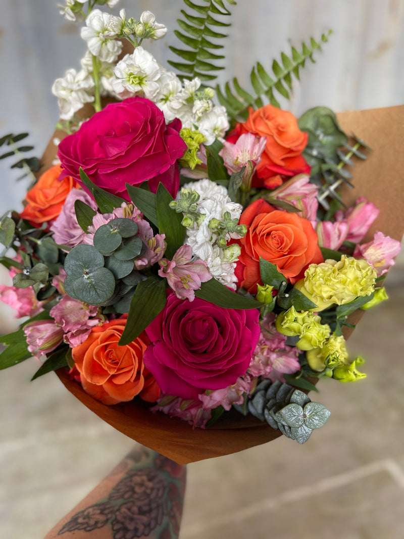 colorful bouquet wrapped in brown kraft paper held by a tattooed arm