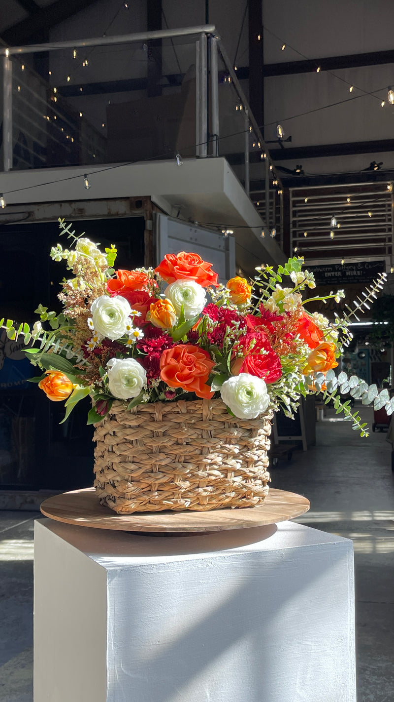 neutral basket filled with colorful flowers on a white pedestal 