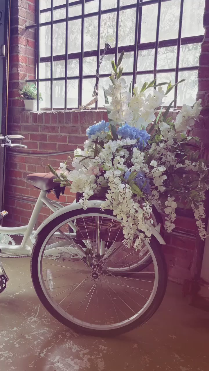 Load video: Introducing our flower bike adorned with flowers creating the perfect photo backdrop and prop! Available to rent, or just snap a photo while visiting!